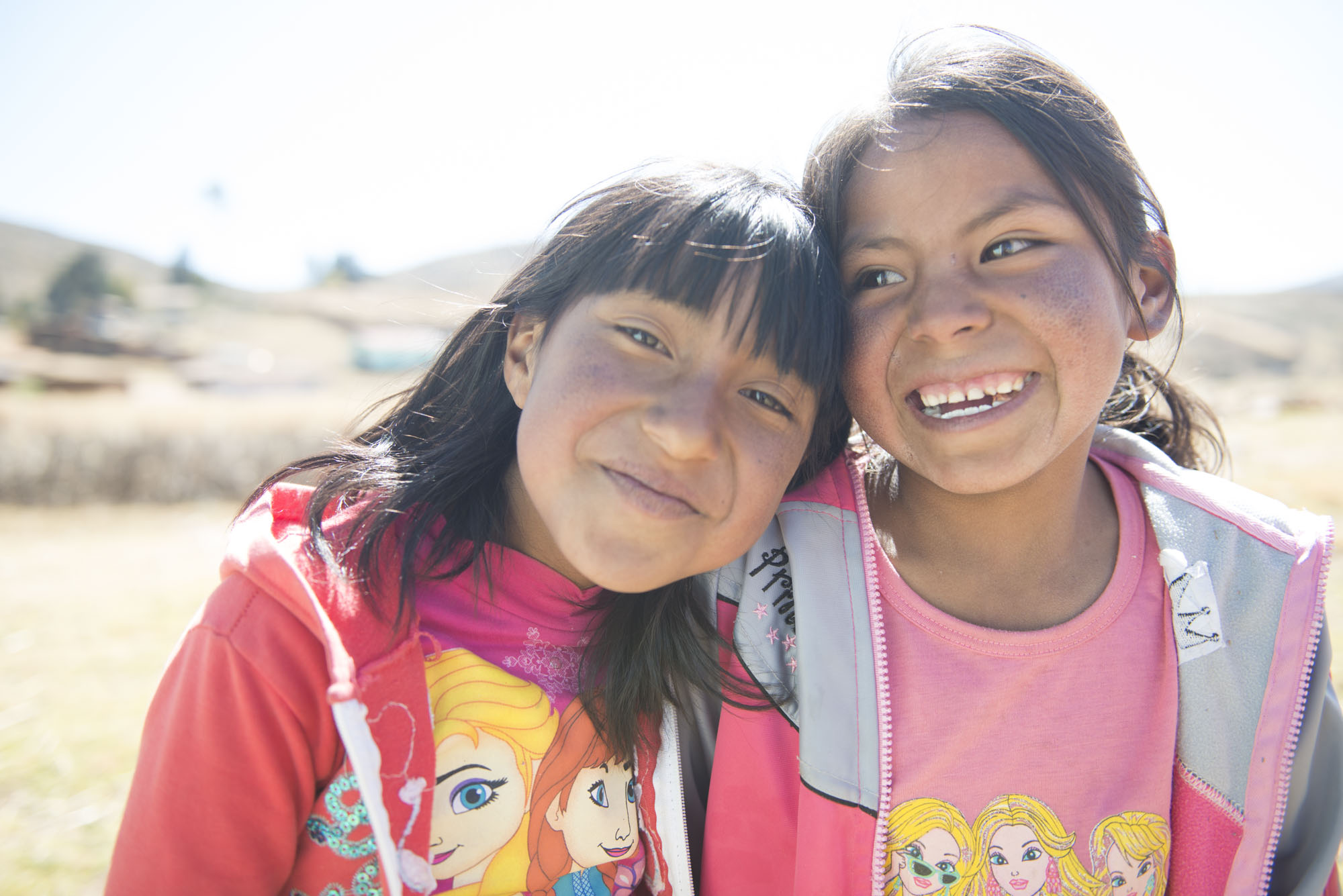 Two young Quechua girls laugh in a field.